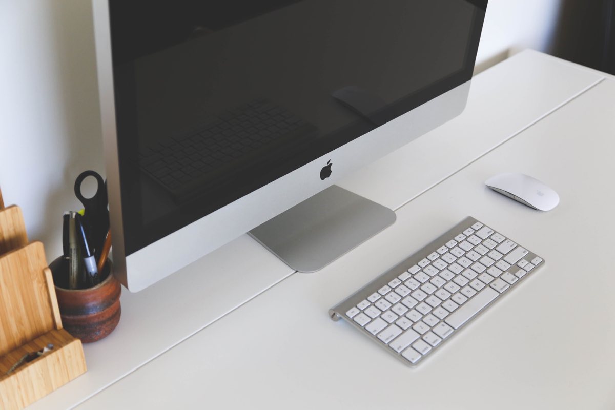 Schreibtisch mit Apple iMac, Tastatur, Maus, Stifthalter und Ablagen.