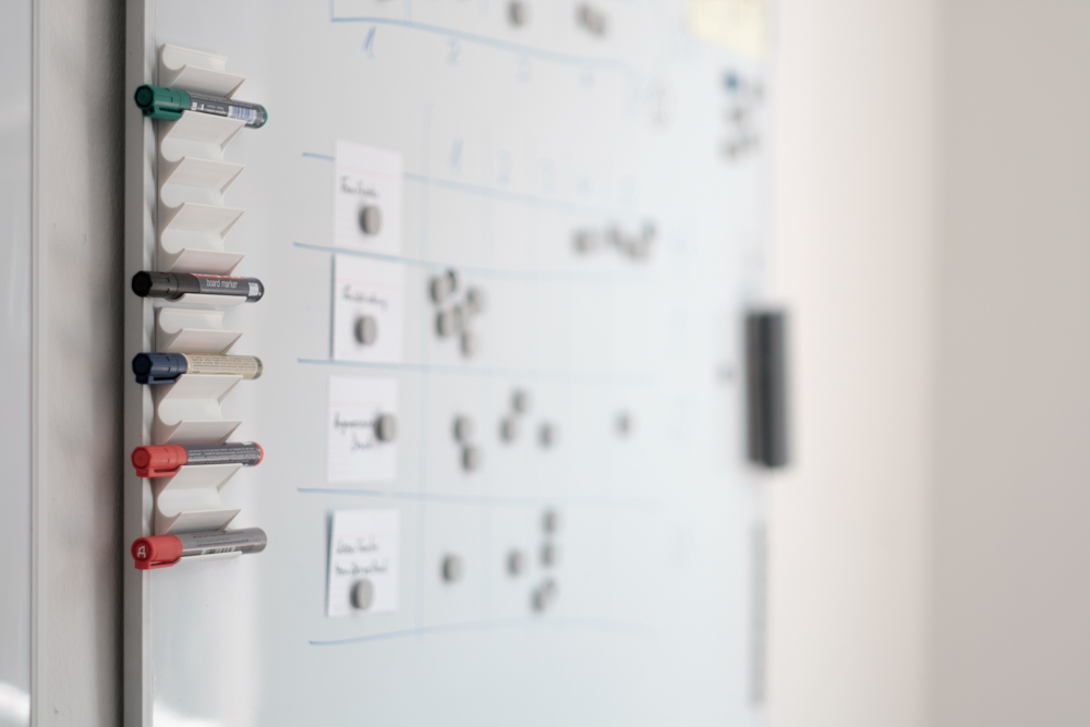 Whiteboard mit Stiften in verschiedenen Farben und teilweise unleserlichen Notizen.